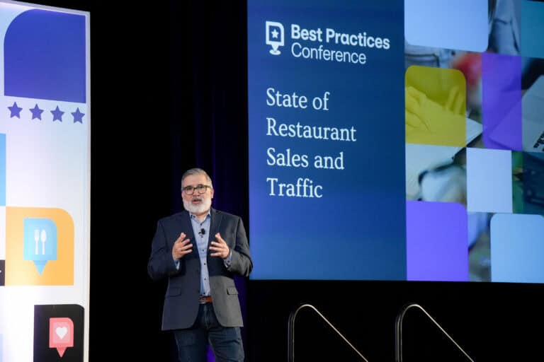 A man stands on a stage giving a presentation at the "Best Practices Conference." A large screen behind him displays the text "State of Restaurant Sales and Traffic" alongside various images collaged together.