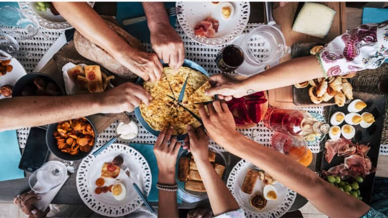 Hands reach across a table of food to serve themselves