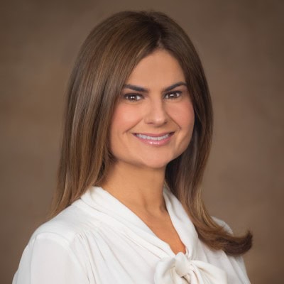 Portrait of a woman - Simone Ventura, Director of Customer Solutions at Bacardi - with shoulder-length brown hair wearing a white blouse. She is smiling against a plain brown background.