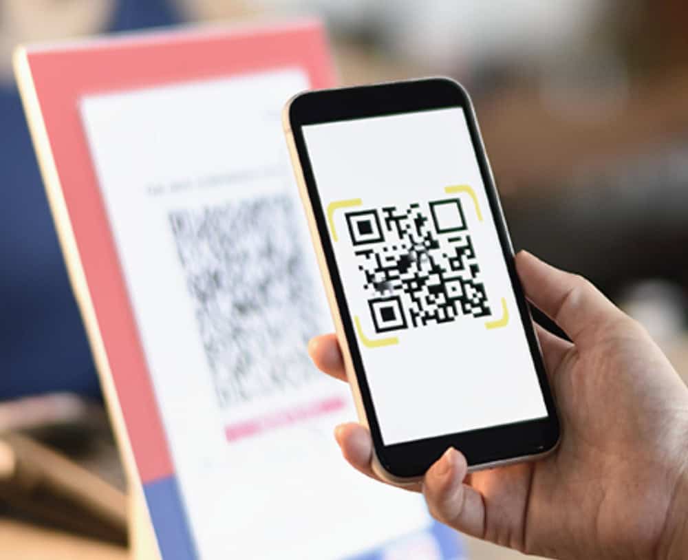 A person holds a smartphone displaying a QR code for Restaurant Survey Collection, scanning or showing it in front of a blurred background with another QR code on a stand.