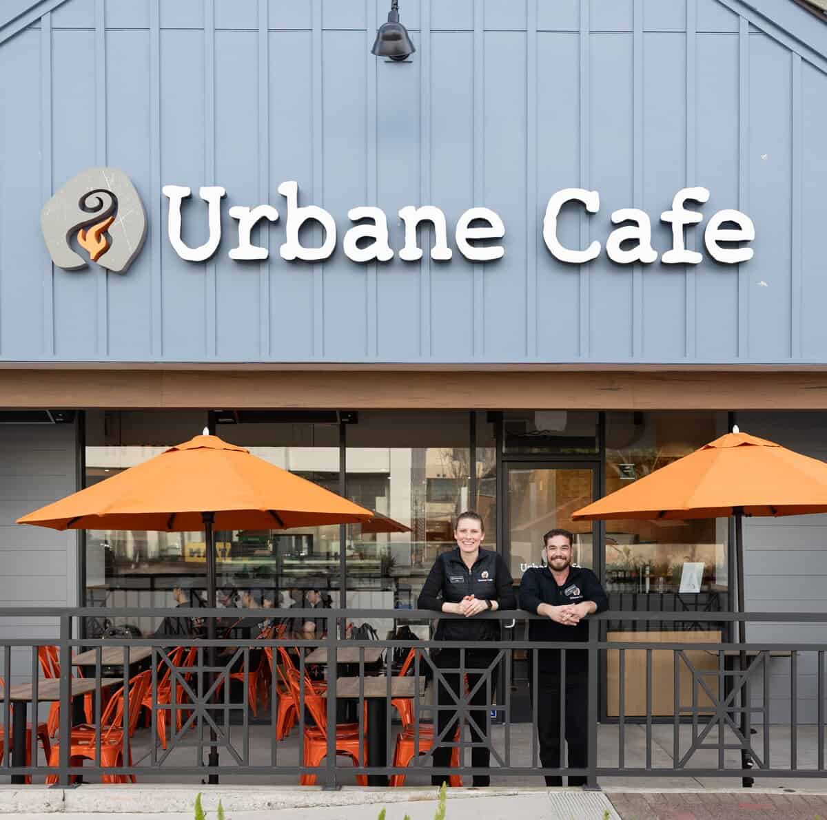 Two people stand in front of Urbane Cafe, a restaurant with a blue exterior, orange umbrellas, and orange chairs on the patio. The Case Study:Urbane Cafe name is displayed in large white letters above them.