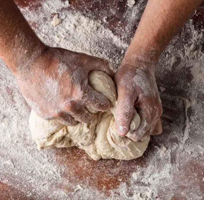 Hands kneading dough on a floured wooden surface, capturing the focus and dedication that helped Case Study: The Restaurant Group achieve NPS and sales growth with BBI Survey Studio. Flour is scattered as the dough is firmly pressed and folded.